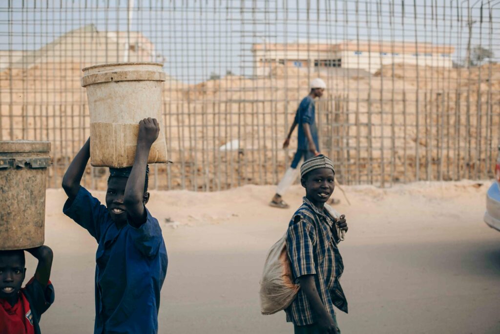Three young boys carrying buckets on a busy outdoor street scene, showcasing daily life.